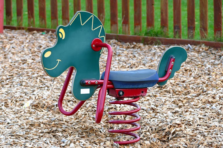 A colorful dinosaur-themed spring rider in an outdoor playground with wood chips.